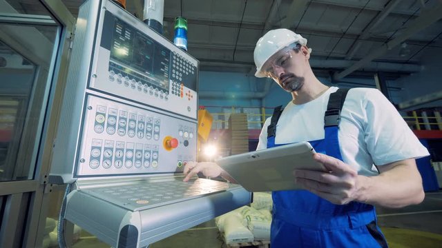 Factory employee is operating a tablet and a monitoring console