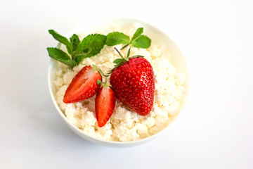 A plate with fresh cottage cheese, strawberries and mint stands on a white background