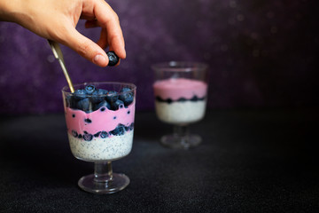 Healthy breakfast chia pudding with blueberries, Greek yogurt and natural blueberry yogurt. Female hand holding chia pudding. Healthy food, vegetarian concept. Dark purple background