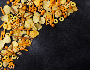 Different types of snacks, chips, nachos, nuts, potato and corn chips, beer snacks. Black background. Top view. Copy space