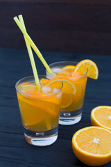 Alcoholic and non-alcoholic citrus drink with orange and lemon in glasses on a dark wooden background