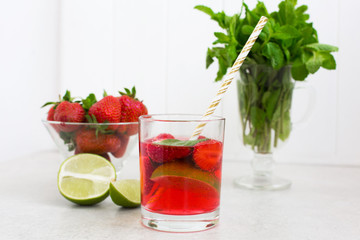 Cold fresh strawberry cocktail in a glass with ice and mint, an inverted  bowl with strawberries and lime slices.