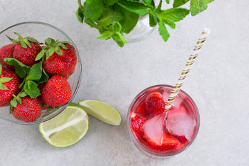 Cold strawberry cocktail in a glass with ice and mint, a bowl with strawberries and lime slices 