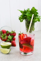 strawberry cocktail in a glass with ice and mint, a bowl with strawberries and lime slices