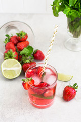 strawberry cocktail in a glass with ice and mint, a bowl with strawberries and lime slices