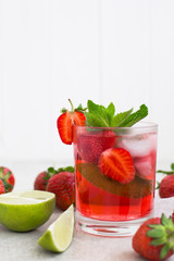 On  gray background there is a strawberry cocktail in a glass with ice and mint and lime