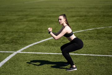 Girl doing a squat at the stadium. Black leggings and top. Football field.