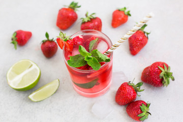 Cooling summer cocktail with strawberries, ice and mint in a glass and around the berries are ripe fresh strawberries and lime