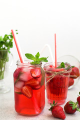 On a light gray background there are a strawberry cocktail in a glass and  bank with ice and mint,  strawberries 