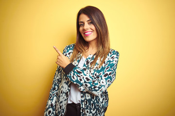Young beautiful woman wearing casual jacket over yellow isolated background cheerful with a smile on face pointing with hand and finger up to the side with happy and natural expression