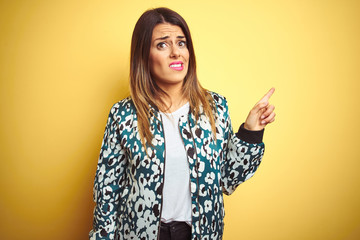 Young beautiful woman wearing casual jacket over yellow isolated background Pointing aside worried and nervous with forefinger, concerned and surprised expression