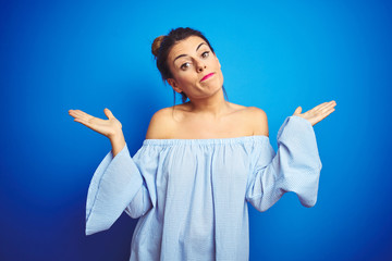 Young beautiful woman wearing bun hairstyle over blue isolated background clueless and confused...