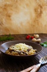 Traditional Italian dish of rice arborio risotto with mushrooms. Served with fresh basil, mushrooms and cherry tomatoes on a dark wooden table. Vertical. Close-up. Light marble background
