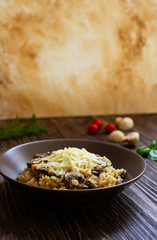 Traditional Italian dish of rice arborio risotto with mushrooms. Served with fresh basil, mushrooms and cherry tomatoes on a dark wooden table. Vertical. Close-up. Light marble background