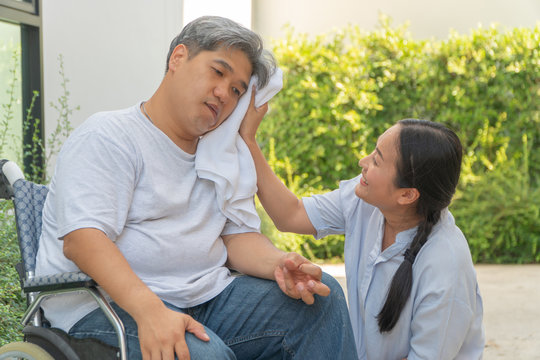 Middle-aged and obese men are paralyzed, Crooked mouth, Crinkled hands and Limb weakness  In the wheelchair and there is a wife using a towel on the face of her husband with love and good hope