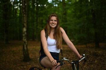 Fototapeta na wymiar Beautiful girl with red hair riding her bike through the forest