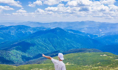 Hiking man pointing on something with his hand. Hipster travelling. Man shows direction with his hand standing on top of cliff in summer mountains.