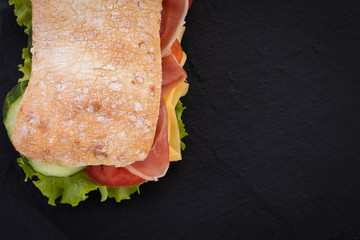 Ciabatta sandwich with lettuce , prosciutto and  cheese over stone background. Top view with copy space