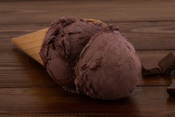 chocolate ice cream scoops in waffle cones and chocolate pieces on wooden background