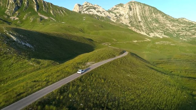 Aerial view of white car driving on mountain serpentine road in sunset lights. Aerial 4K drone shot