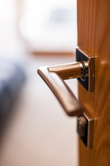High quality stainless steel handle on wooden door opening into modern bright bedroom with big windows