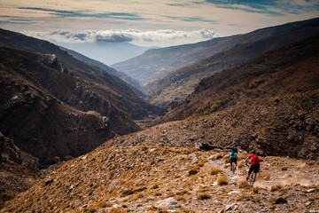 SIERRA NEVADA, SPAIN. Two mountain bikers riding down a rough singletrack trail in a barren remote...