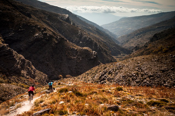 SIERRA NEVADA, SPAIN. Two mountain bikers riding down a rough singletrack trail in a barren remote...