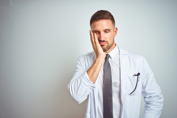 Young handsome doctor man wearing white profressional coat over isolated background thinking looking tired and bored with depression problems with crossed arms.