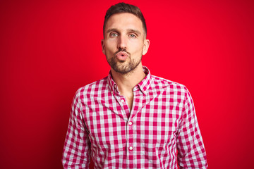 Young handsome man over red isolated background looking at the camera blowing a kiss on air being lovely and sexy. Love expression.