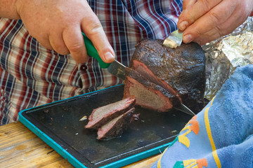 Hand cuts a grilled beef from the grill