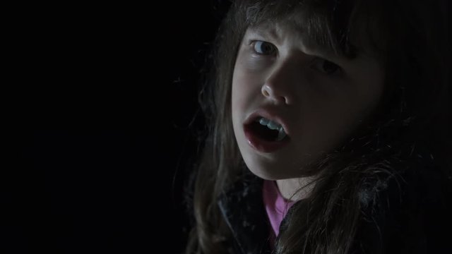 Horror at Halloween day. Angry little girl with dracula teeth in the dark. Halloween child.