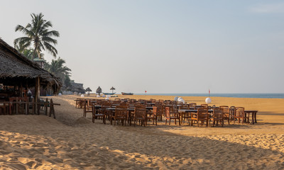 Tropical beach in Mount Lavinia, Sri Lanka with straw umbrellas, chairs and benches on the sands.