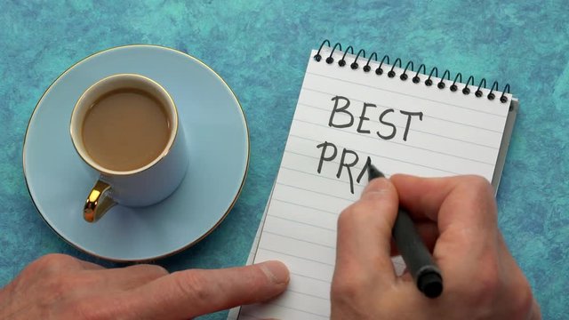 Best practice concept - man hand writing a note with a black marker in a spiral notebook, overhead view