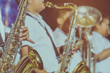 Male student with friends blow the saxophone with the band for performance on stage at night.