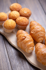 Cupcakes and croissants fresh out of the oven on wooden board. Vertical breakfast shoot.