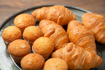 Close-up of cupcakes and croissants on metal tray on brown wooden table. Breakfast.
