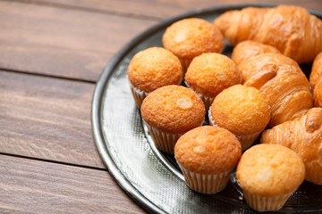 Cupcakes and croissants on metal tray on brown wooden table. Copy space.