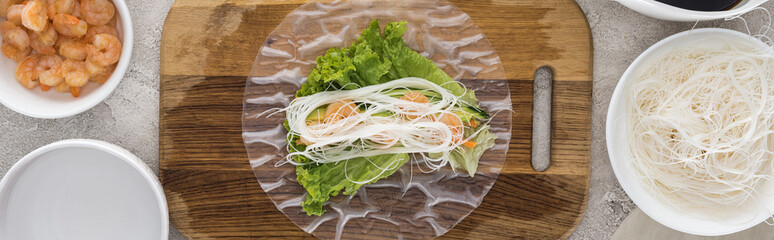 panoramic shot of shrimps, lettuce and noodles on rice paper, on cutting board