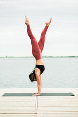 Obraz premium Asian young girl doing yoga outdoors on the pier by the lake.