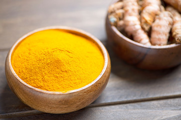 Bowl with turmeric powder in the foreground next to another bowl with turmeric root on brown wooden table. Spice for health and ingredient of Indian cuisine.