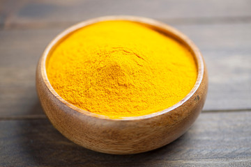 Bowl with curcumin powder on brown wooden table. Spice for health and ingredient of Indian cuisine.