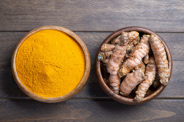 View from above bowl with turmeric powder next to another bowl with turmeric root on brown wooden table. Spice for health and ingredient of Indian cuisine.