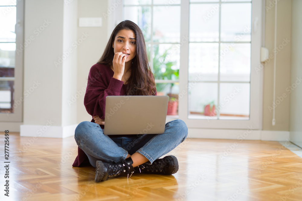 Wall mural young woman using computer laptop sitting on the floor looking stressed and nervous with hands on mo