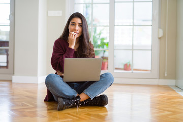 Young woman using computer laptop sitting on the floor looking stressed and nervous with hands on...