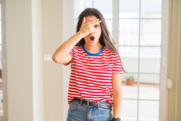 Young beautiful woman wearing casual t-shirt peeking in shock covering face and eyes with hand, looking through fingers with embarrassed expression.