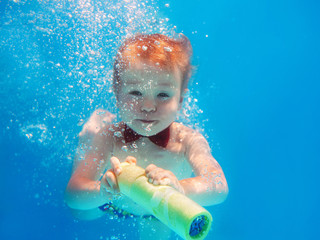 Little funny cheerful child boy with red butterfly and with water gun diving underwater in swimming pool, learn to swim. Sport and vacation concept