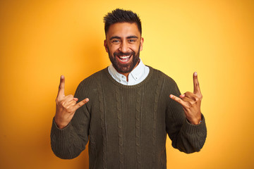 Young indian man wearing green sweater and shirt standing over isolated yellow background shouting...