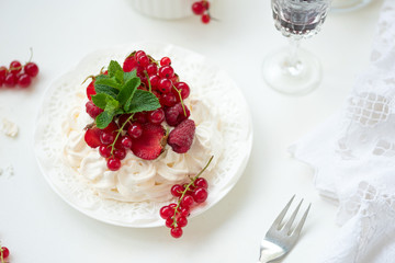 Pavlova fruit cake with strawberry, raspberry, red currant and mint leaves on white background. Selective focus. Healthy food concept