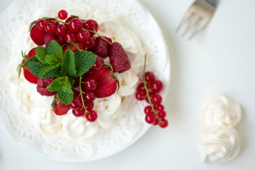 Pavlova fruit cake with strawberry, raspberry, red currant and mint leaves on white background. Selective focus. Healthy food concept