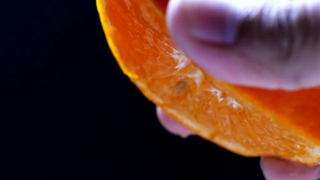 Squeezing orange fruit in slow motion on black background. Health food. Close-up. Macro